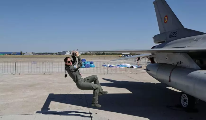 Bianca Botaș, în combinezon, lângă avionul său F-16 Fighting Falcon, cu aeroportul Băneasa pe fundal.