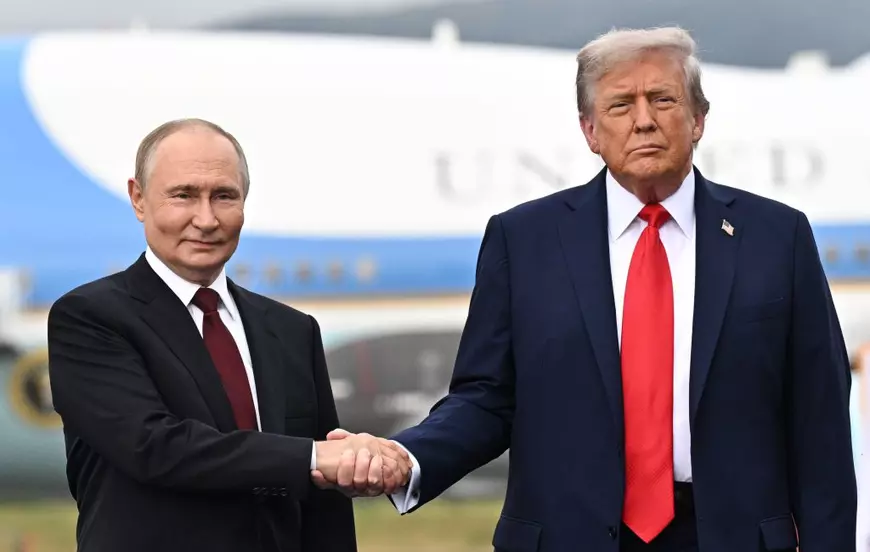 Vladimir Putin (stânga) și Donald Trump (dreapta) surprinși în timp ce-și strâng mâinile vineri, 15 august 2025, în Alaska