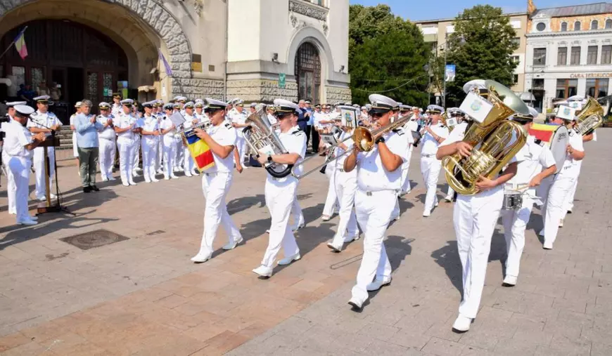 Paradă militară cu ofițerii Forțelor Navale Române în timp ce fanfara cântă în centrul orașului Constanța, militarii poartă uniforme albe