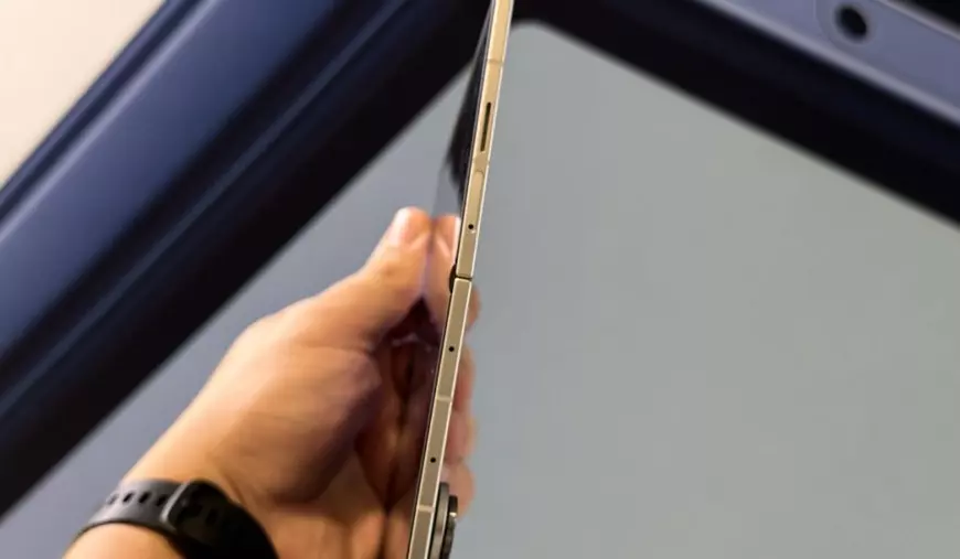 Partea laterală a unui telefon Samsung Galaxy Z Fold7 gri, ținut în mână în fața unui fundal gri.