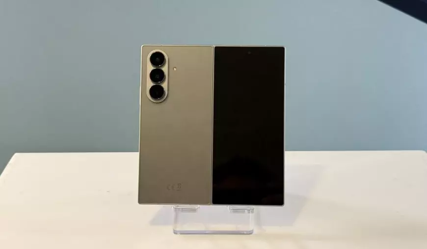 Partea din spate a unui telefon Samsung Galaxy Z Fold7 gri, așezat pe un stand de prezentare în fața unui fundal vernil.