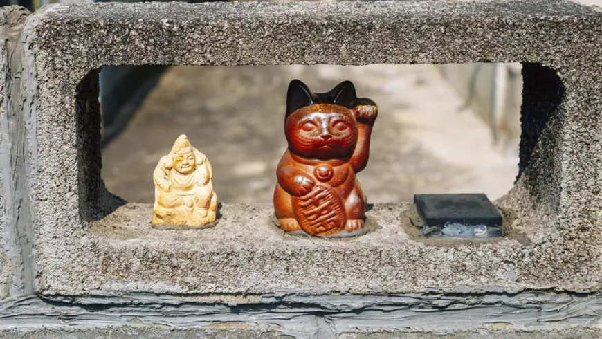 Pisică norocoasă japoneză maneki neko, maro, tine labuta stanga ridicata, în satul japonez vechi Uchiko din orașul Ehime, Shikoku, Japonia, Asia