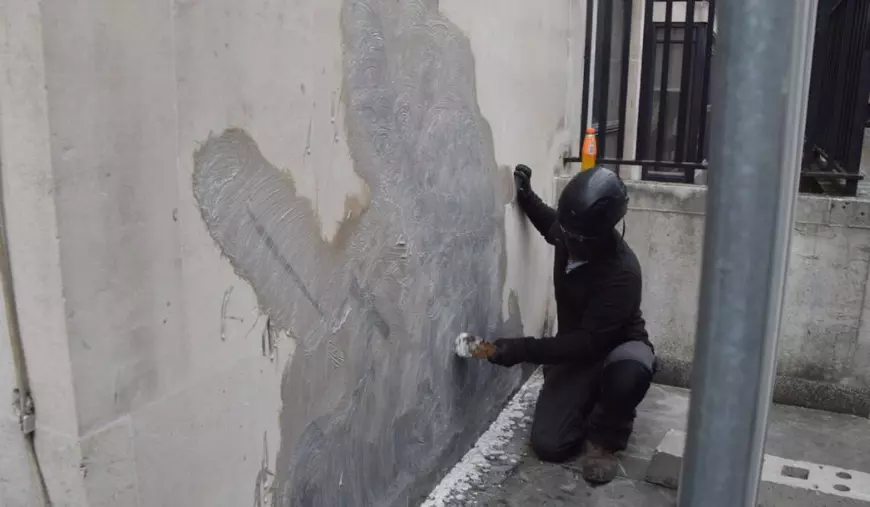 Un muncitor ]mbrăcat în negru complet si cu fața acoperită curăță cea mai recentă operă de artă a evazivului artist stradal Banksy de la Curtea Regală de Justiție, care înfățișează un judecător lovind un protestatar cu un ciocan, după ce instanța a ordonat îndepărtarea acesteia. 10 septembrie 2025