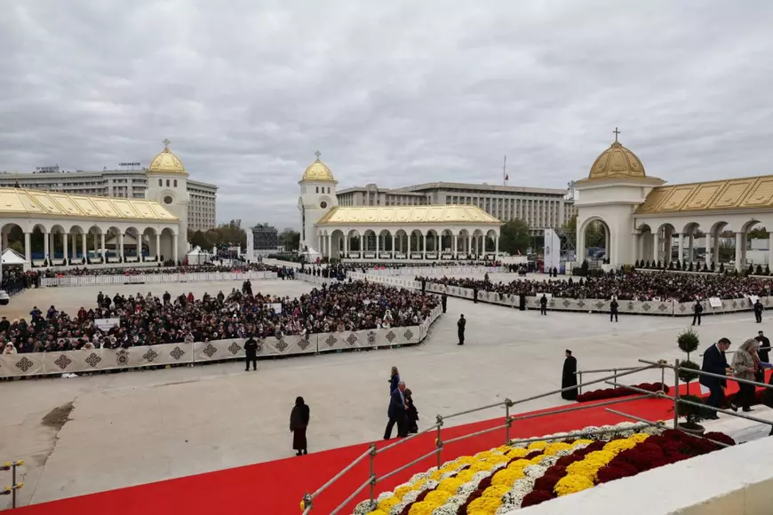 Ceremonia de sfințire a picturii Catedralei Mântuirii Neamului. In curtea catedralei oamenii sunt organizati si stau in grupuri in zone special amenajate intr-o ordine care impresioneaza