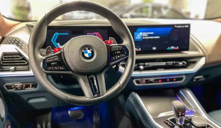 Interiorul unei mașini BMW nouă, bordul autoturismului are ecranul pornit, cutia de viteze este automată. Sigla BMW este montată în interiorul volanului