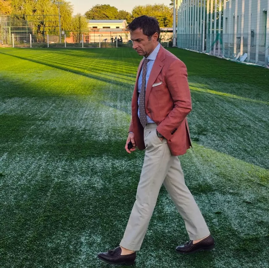 Radu Cristian, primarul municipiului Mangalia, imbracat in sacou corai, pantaloni crem, se plimba pe un gazon verde