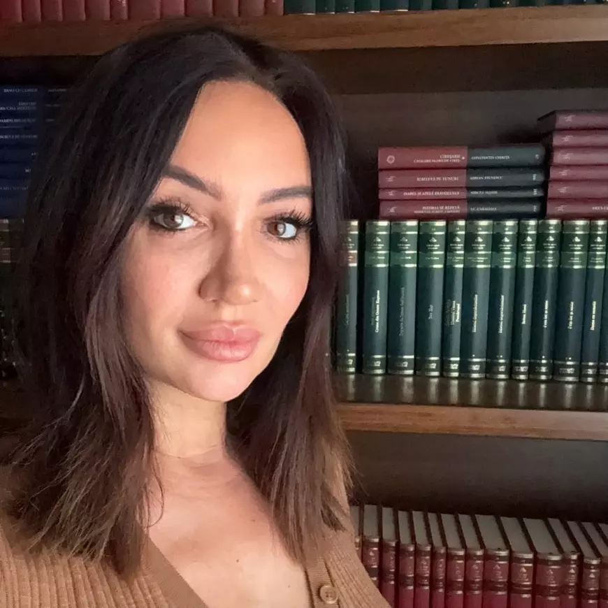 O tanara satena stă lângă o bliblioteca plina de carți