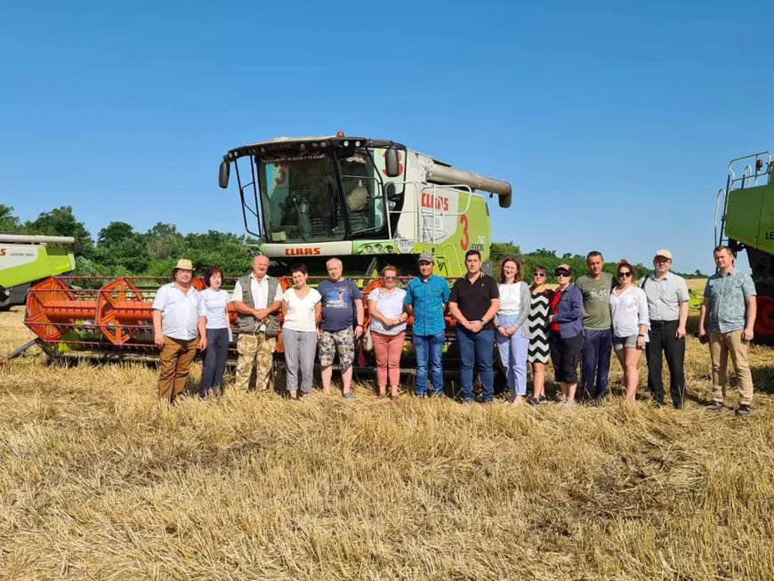 Mai multi lucrărori pe un camp agricol in fata unei masini aglicole