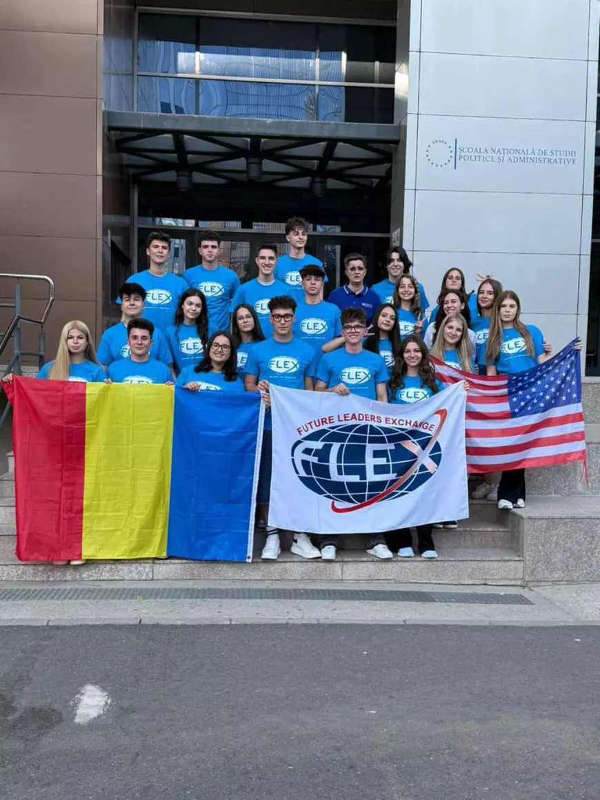 Mai mulți elevi, îmbrăcați cu tricouri albastre, pozează cu steagurile României, Americii și un steag alb pe care scrie Flex