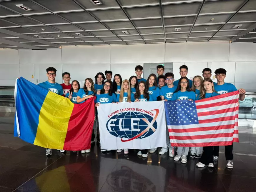 Mai mulți elevi, îmbrăcați cu tricouri albastre, pozează cu steagurile României, Americii și un steag alb pe care scrie Flex