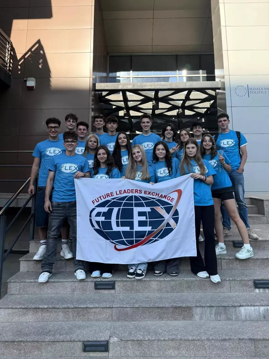 Mai mulți tineri, îmbrăcați în tricouri albastre, pozează pe niște scări, si arată un steag alb pe care scrie FLEX