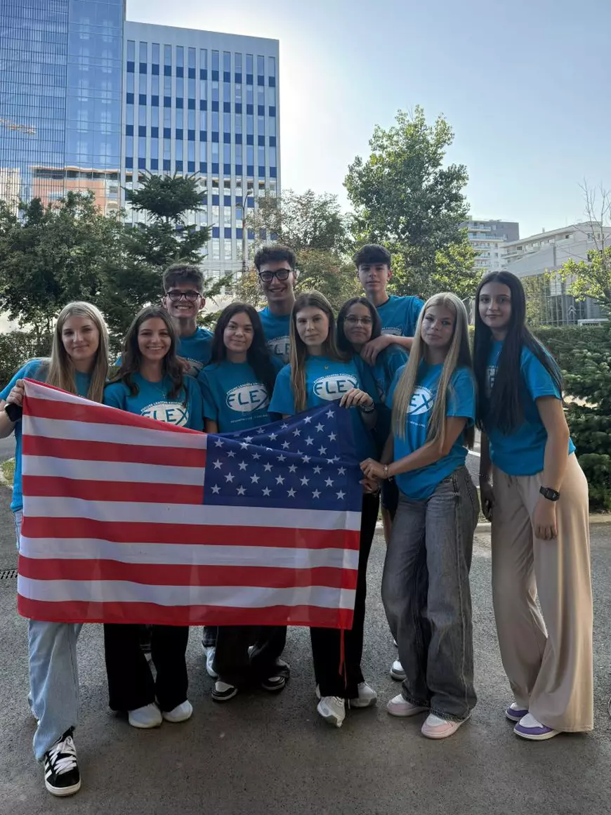 Mai mulți elevi, îmbrăcați cu tricouri albastre, pozează cu steagurile Americii