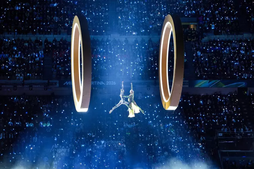 Moment de la ceremonia de deschidere a JO de Iarnă 2026, 2 acrobați coboară de la înălțime între 2 cercuri olimpice uriașe