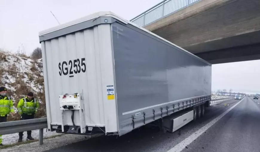 O semiremorca avariată, în poziția sa finală, in dreptul unui pod, in spatele ei doi politisti cu geci verzi se uita curiosi, pe margine se vede zăpadă