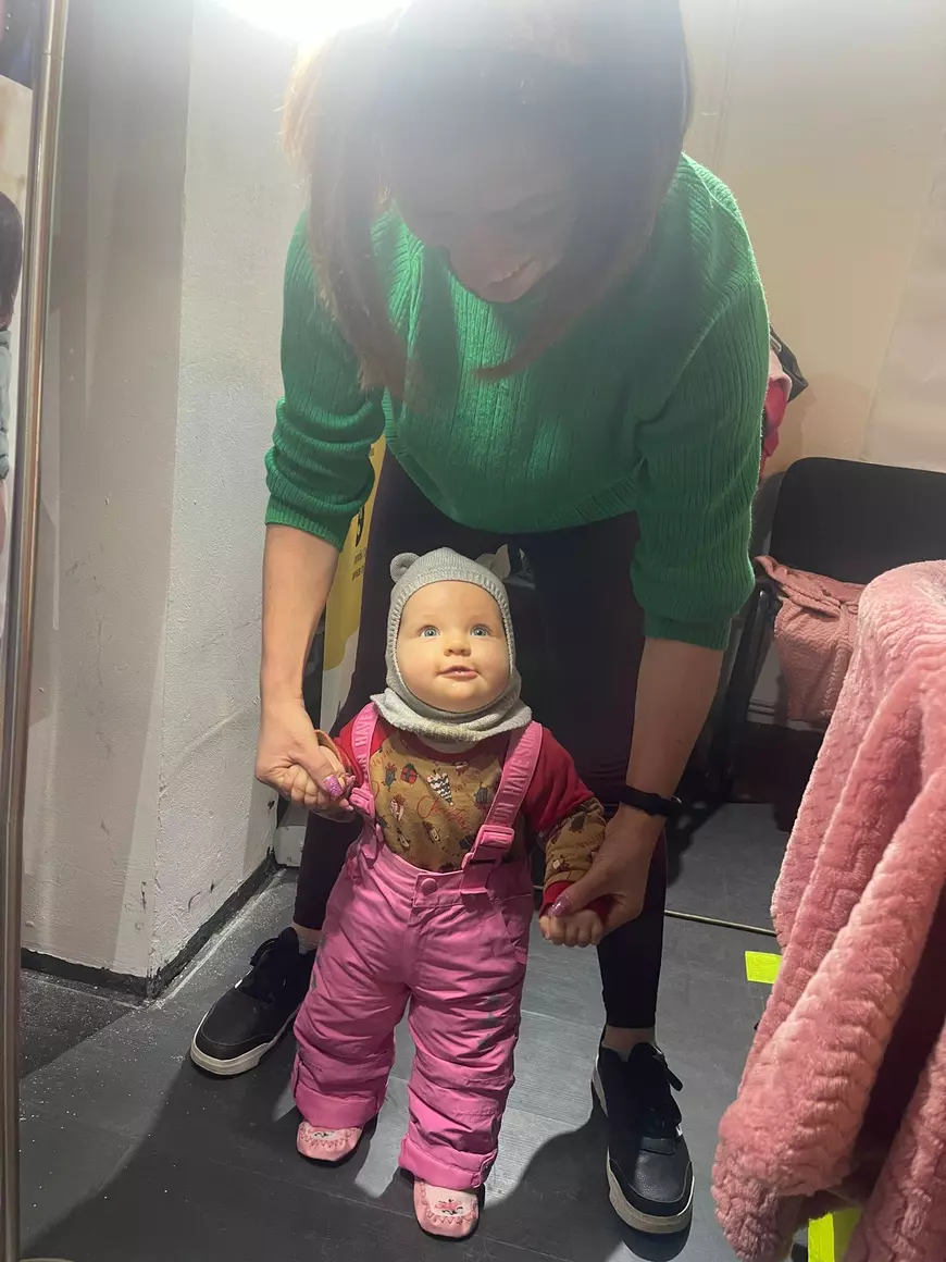 O mamica imbracata in verde tine de maini o fetita in roz care face primii pasi