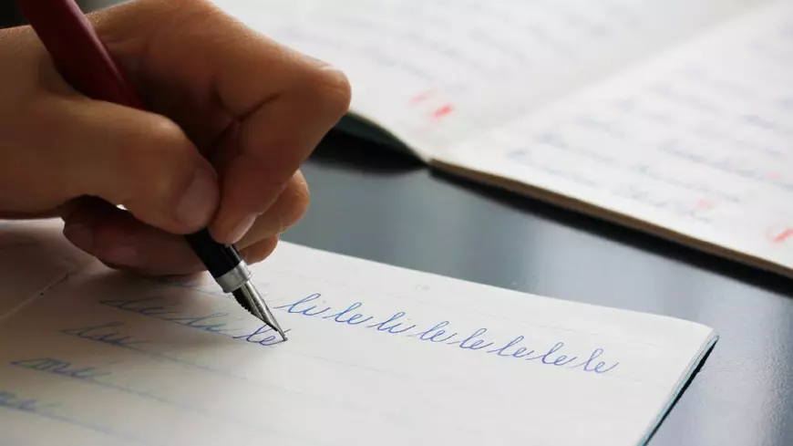 Un copil care scrie silabele li și le cu un stilou într-un caiet.