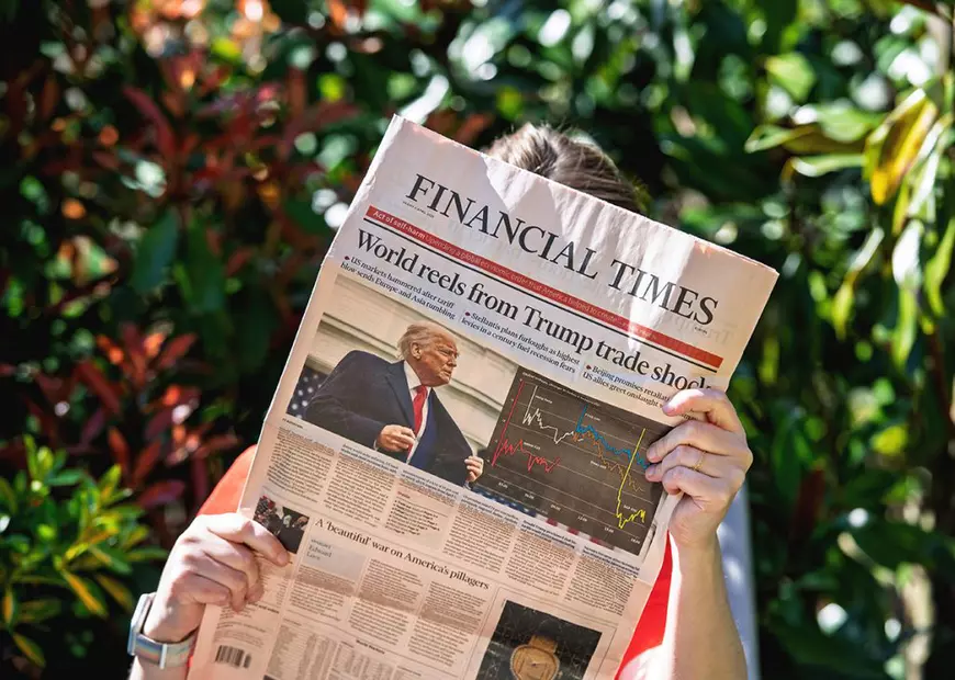 Paris, Franța - 9 aprilie 2025: O persoană îmbrăcată într-o cămașă roșie ține un ziar Financial Times într-o grădină, cu un titlu pe prima pagină a politicilor comerciale ale lui Trump, cu fotografia sa și hărțile de piață vizibile
