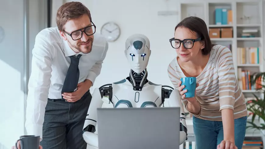 Un robot incadrat de doi programatori se uita la ecranul unui computer