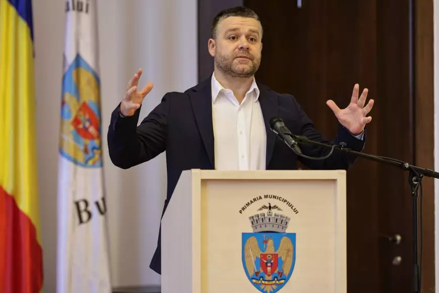 Ciprian Ciucu, cu mâinile întinse, îmbrăcat în sacou negru și cămașă albă, la o conferinta de presă pe 26 martie 2026