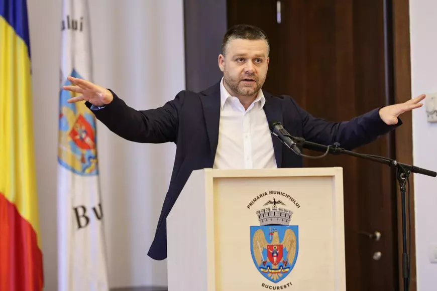 Ciprian Ciucu, cu mâinile întinse, îmbrăcat în sacou negru și cămașă albă, la o conferinta de presă pe 26 martie 2026