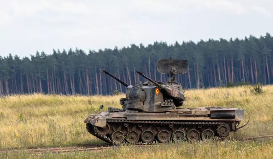 In imagine Gepardul german, un sistem de tun antiaerian autopropulsat construit pe șasiul tancurilor Leopard 1, cu tunuri și radar twin de 35 mm, pe camp, iarba inalta, in spate o padure