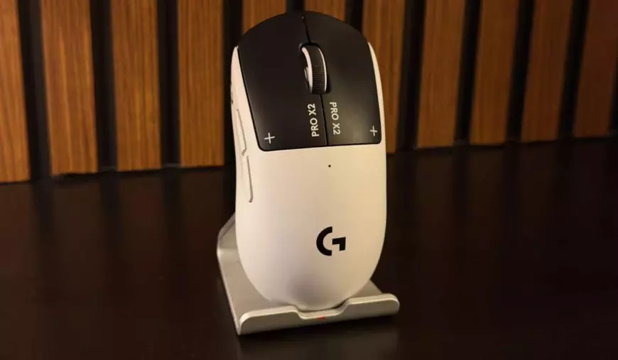 Prim-plan cu mouse-ul Logitech Pro X2 Superstrike, de culoare albă, cu click-uri negre și fundal de lemn.