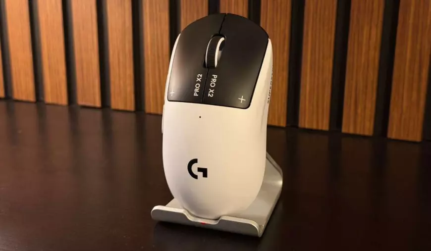 Prim-plan cu mouse-ul Logitech Pro X2 Superstrike, de culoare albă, cu click-uri negre și fundal de lemn.