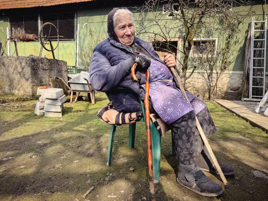 O femeie in varsta sta pe un scaun cu doua carje in maini