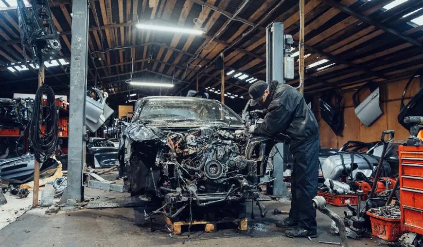Un mecanic lucrează într-un service auto la o mașină avariată