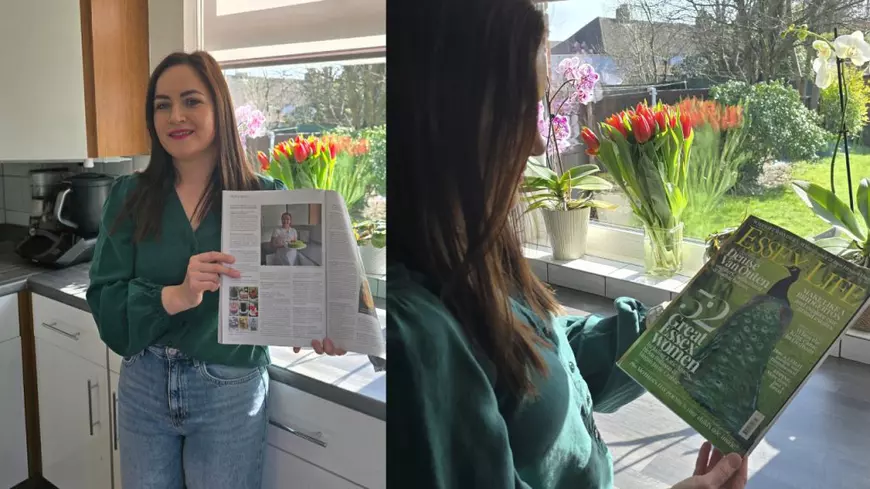 O femeie în bluză verde pozează cu o revistă, în bucătărie