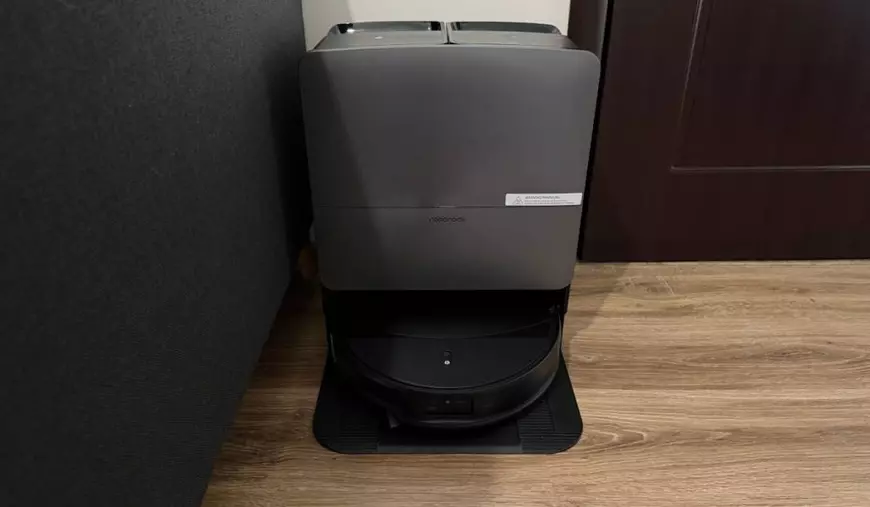 Prim-plan cu aspiratorul robot negru Saros 20 de la Roborock, în timp ce stă în docul de curățare și încărcare, pe un parchet de culoarea lemnului.