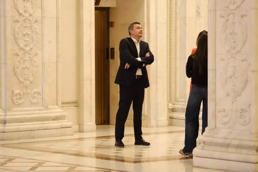 Sorin Grindeanu, liderul PSD, îmbrăcat în costum negru, stă cu mâinile în sân, pe holurile Parlamentului, 19 martie 2026
