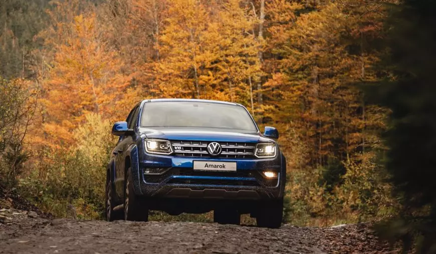 Camioneta Volkswagen Amarok conducând pe teren accidentat la apusul soarelui de vară. Fundal de toamnă