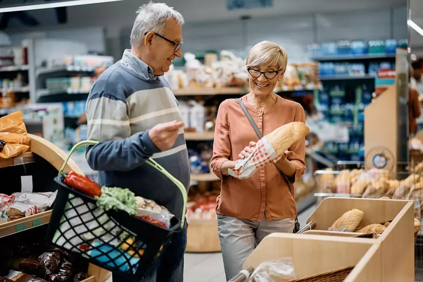O femeie în vârstă fericită și soțul ei luând pâine în timp ce fac cumpărături la supermarket