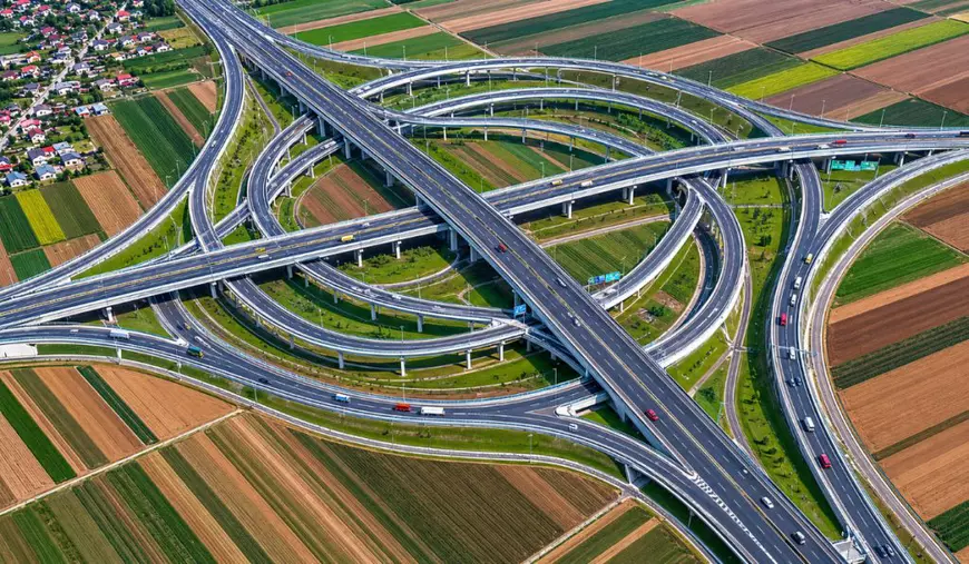 Imaginea prezintă randarea unui proiect uriaș de infrastructură, un nod rutier cu mai multe etaje, bretele și pasaje, pe care circulă mai multe vehicule