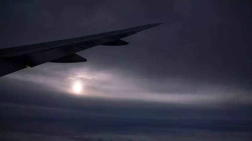 O vedere de la geamul unui avion British Airways care zboară deasupra sudului Angliei, pe un cer închis, iar în depărtare se vede soarele