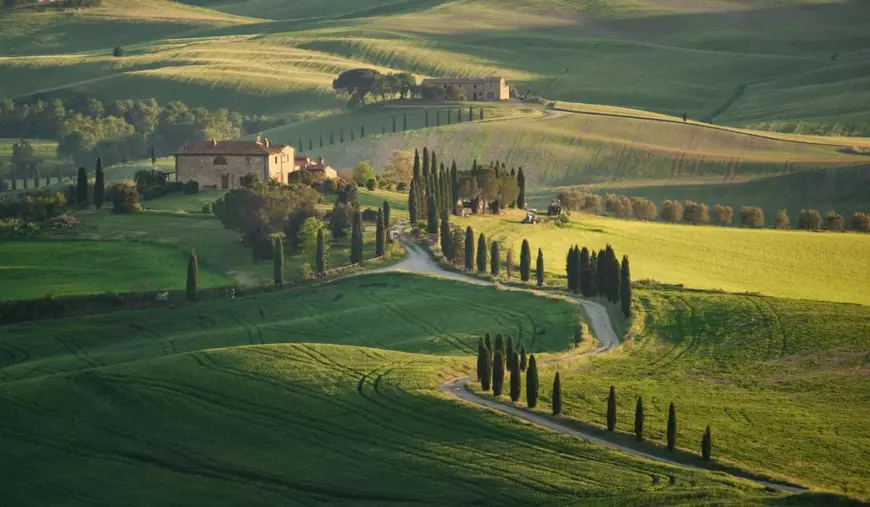 Pienza, Siena, Italia - Mai 01 2025: drum rural căptușit cu chiparoși care duce la o fermă în dealurile verzi rulante din Val d'Orcia, Toscana la apus