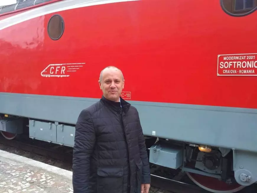 Valentin Dorobanțu îmbrăcat într-o geacă neagră stă în fața unei locomotive roșii.