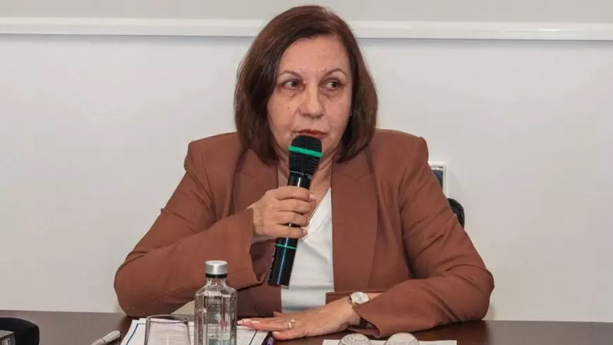 Șefa ANM, Elena Mateescu, îmbrăcată cu o bluză albă și un sacou maro, stă la o masă și vorbește